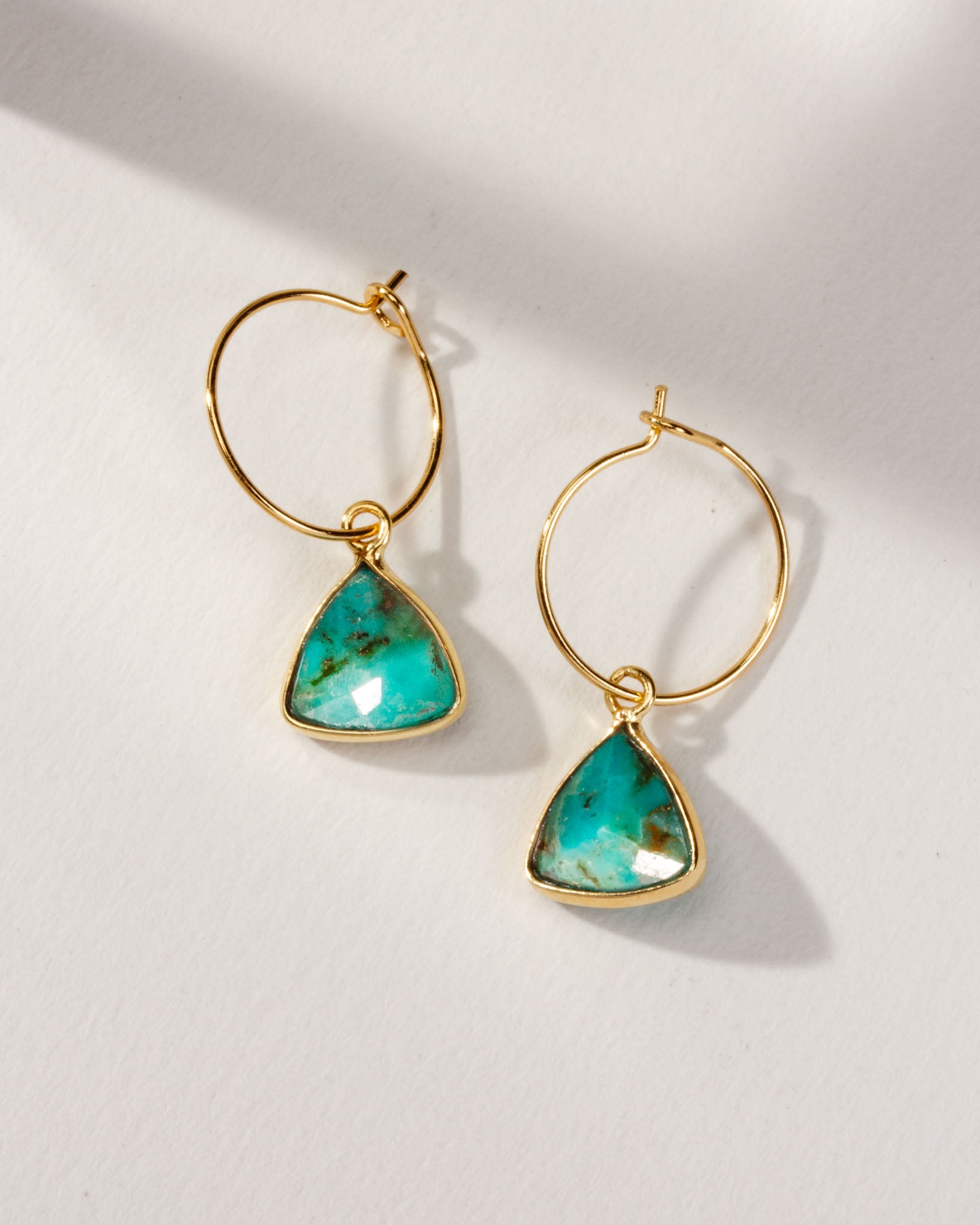Two gold Bermuda Triangle Mini Hoops with turquoise stones are on a white surface.