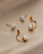 Four Ebb and Flow earrings are scattered on a beige surface; druzy studs and pearl drop backs.