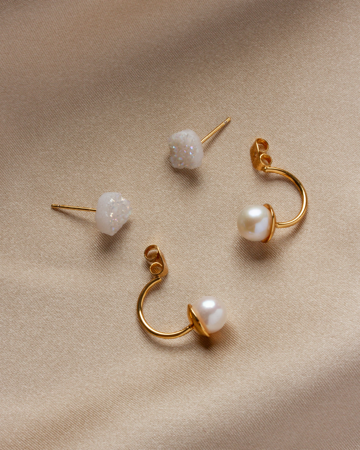 Four Ebb and Flow earrings are scattered on a beige surface; druzy studs and pearl drop backs.