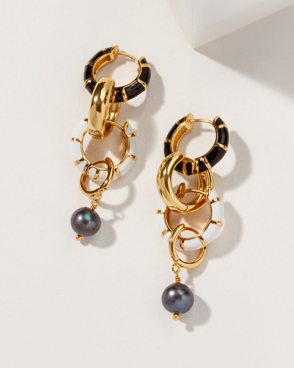 Pair of Jump Through Hoops earrings with black, white, and gold hoops and a dangling dark pearl.