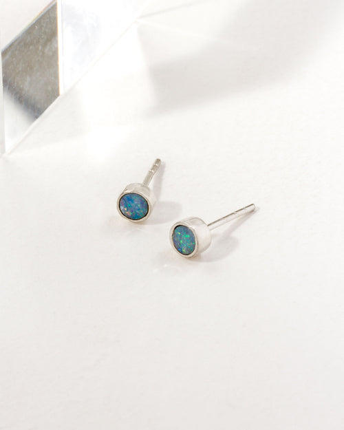 Two round Blue Wave Opal post earrings, bezel set in sterling silver, rest on a white surface.