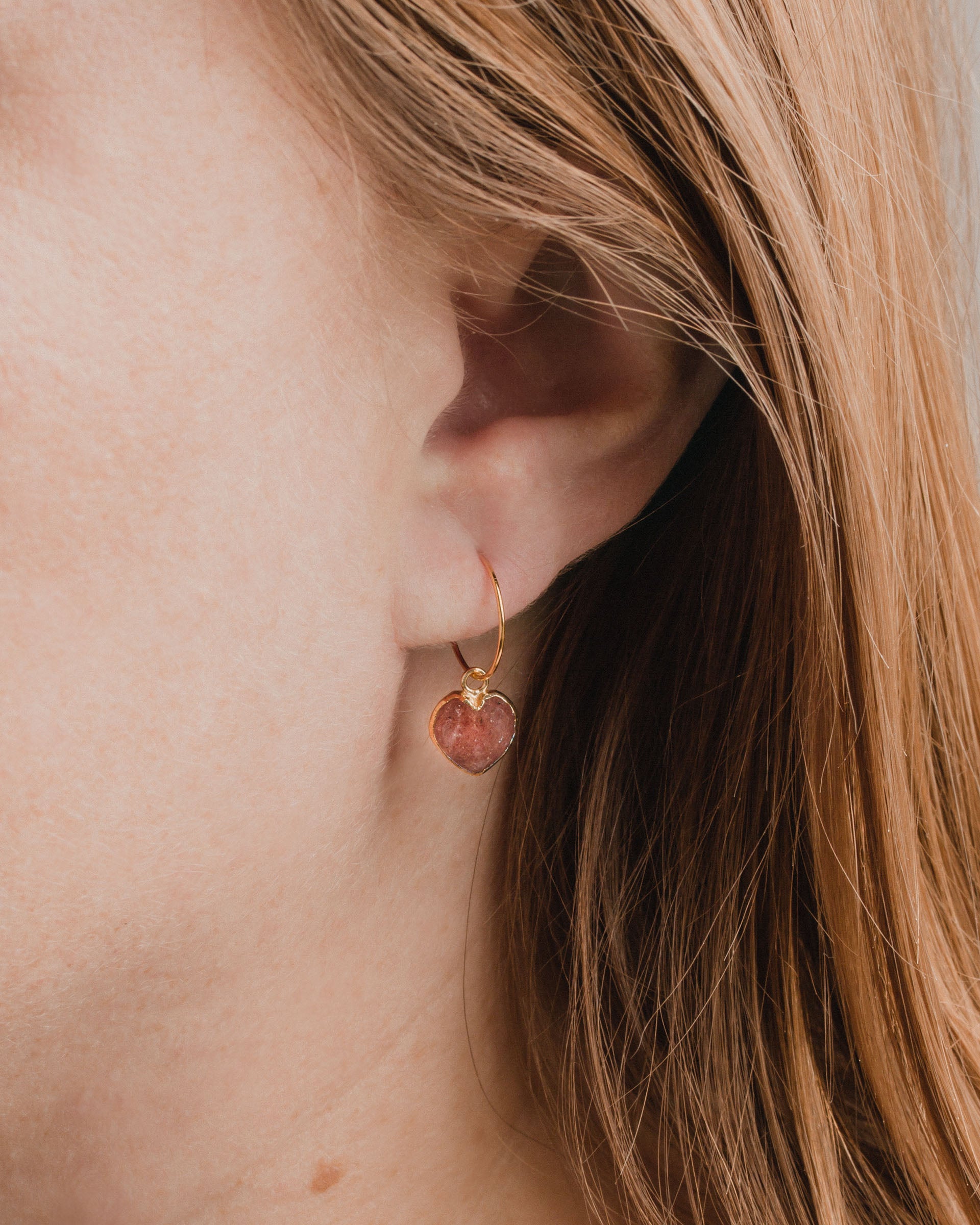 Close-up of a gold Conversation Heart Mini Hoop Earring in Strawberry Quartz on a model.