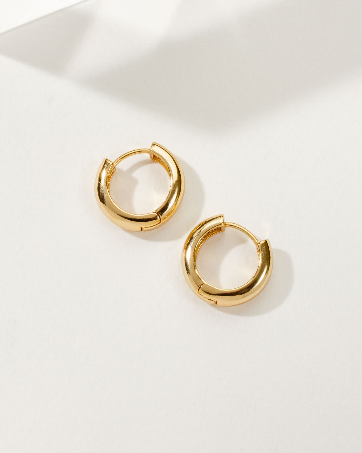 Pair of gold Huggie Hoop Earrings on a white background.