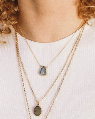 Closeup of a woman’s neckline wearing the Kyanite Earth, Wind, and Fire necklace by Luna Norte Jewelry layered with two other longer length necklaces.