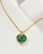 Emerald, heart shaped charm necklace on a white background.