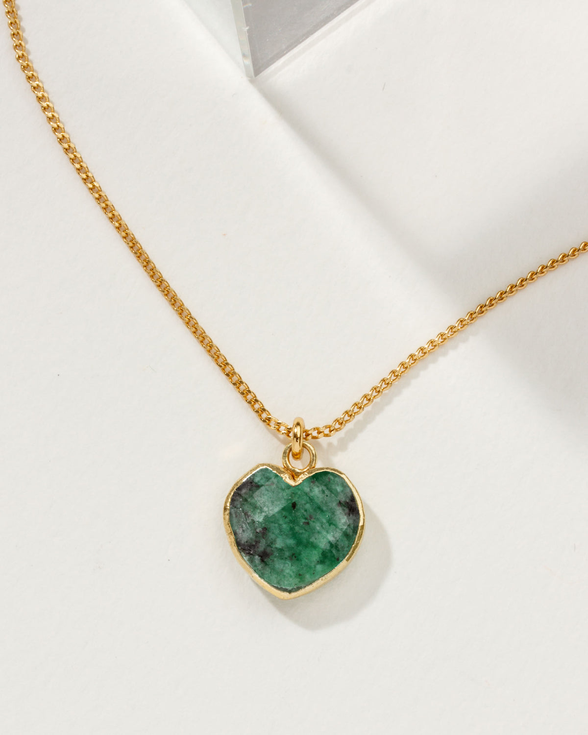 Emerald, heart shaped charm necklace on a white background.