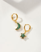 Pair of mismatched gold huggie hoop earrings with emerald star and moon charms
