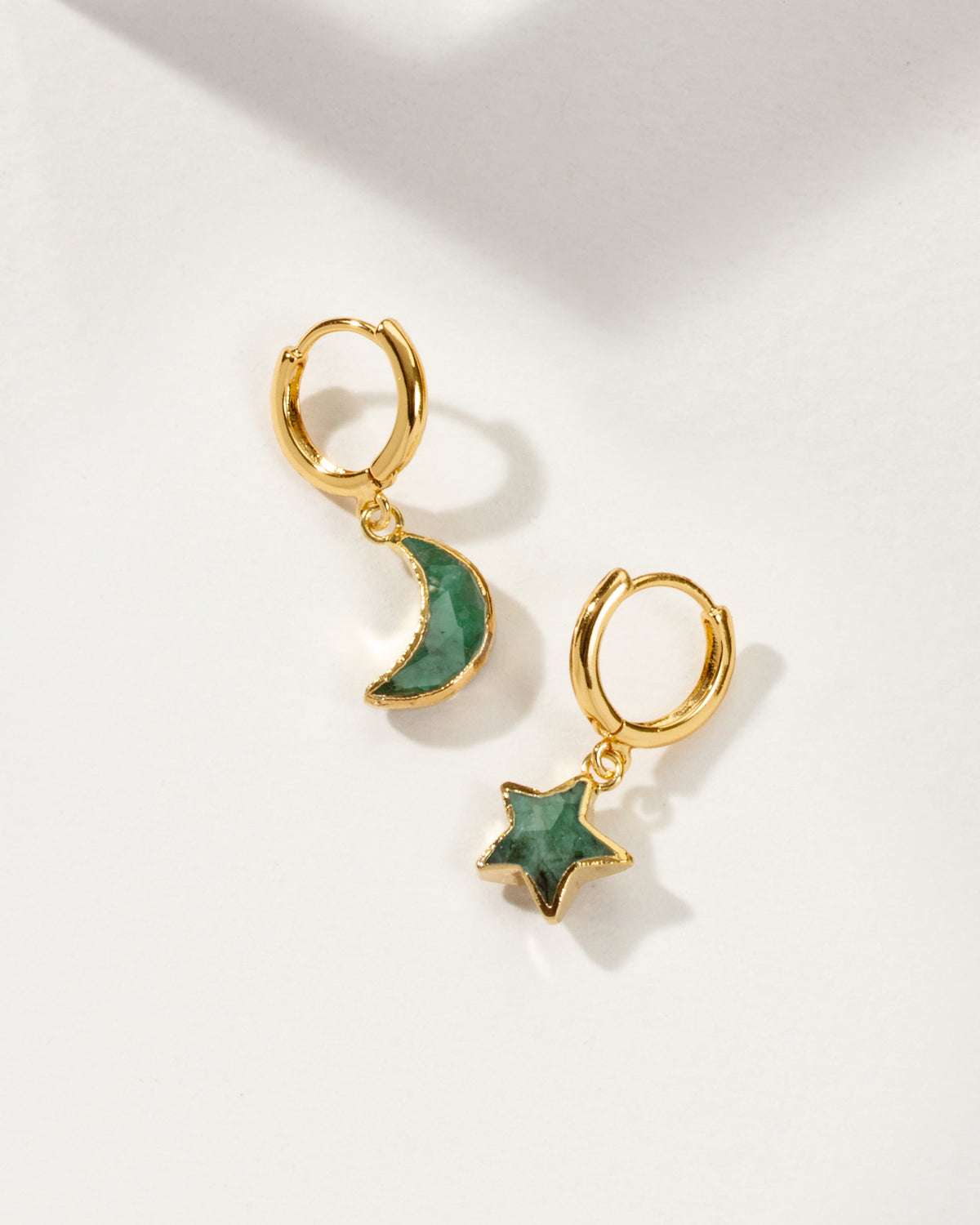 Pair of mismatched gold huggie hoop earrings with emerald star and moon charms