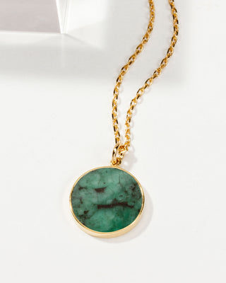 A gold chain necklace with a round, gold-framed emerald medallion pendant featuring a blue-tinted glass surface, displayed against a white background.