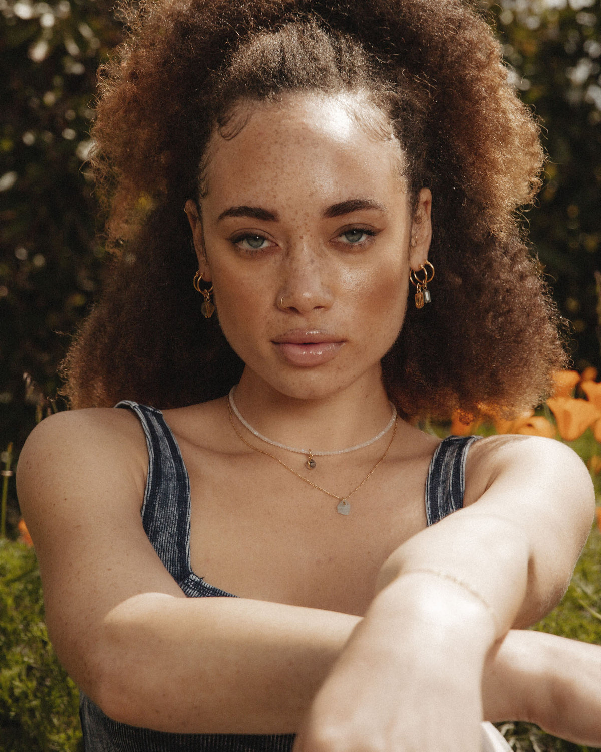 The model wears a Moonstone Flower Petal Necklace, layered with gold earrings and a nose ring.