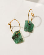 Geometry Mini Hoops in Emerald, with two green, geometrically cut stones hanging from gold hoops.