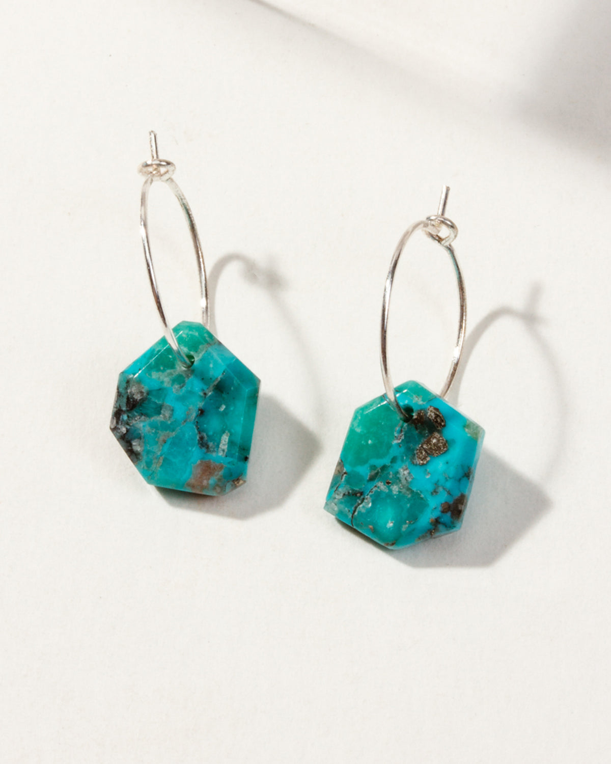 Sterling Silver Geometry Mini Hoops with Turquoise gemstones on a white surface.