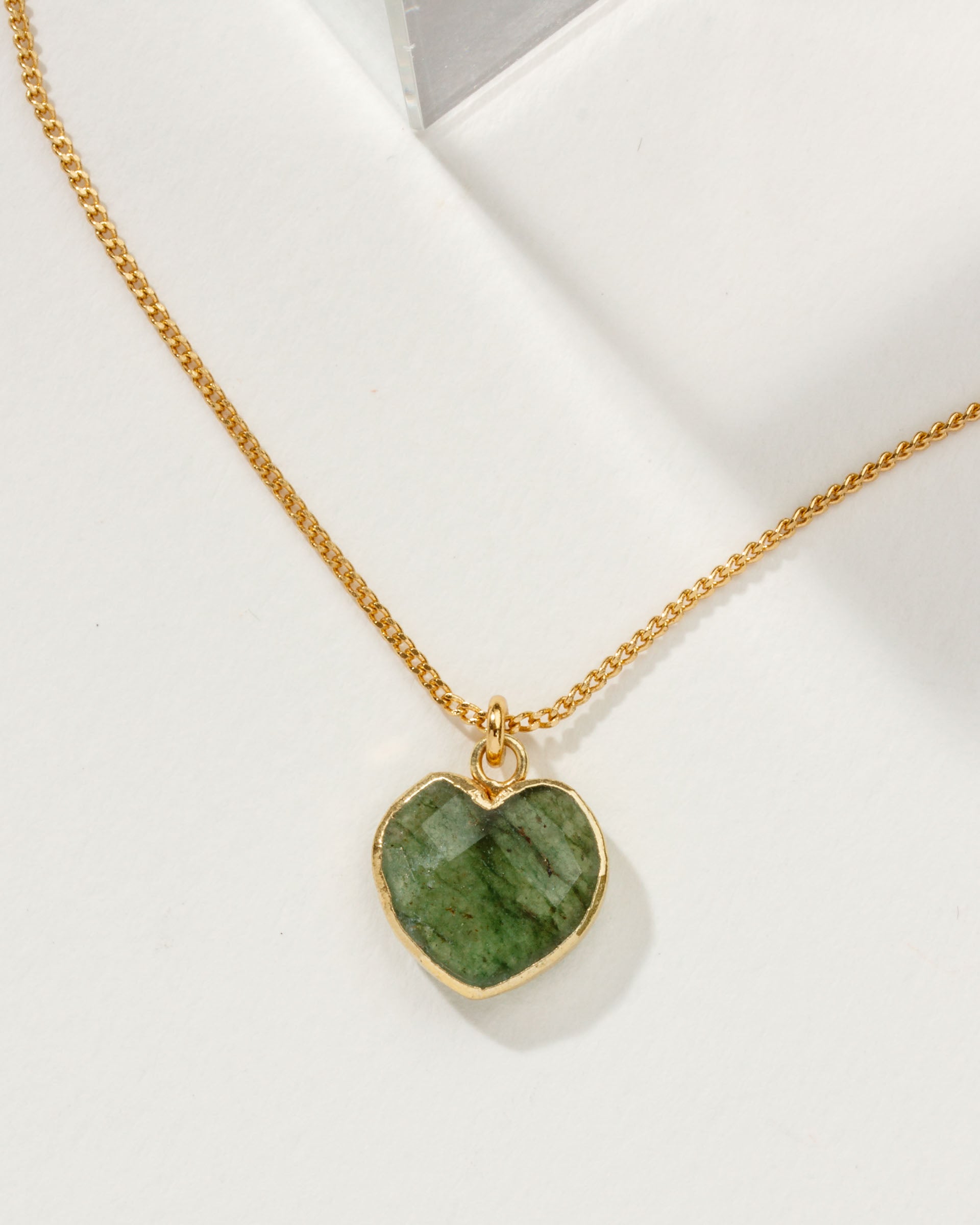 Green aventurine heart-shaped gemstone pendant on a gold chain against a white background.