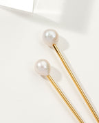 Two pearl hair pins with gold shafts lay diagonally on a white surface.