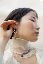 Jump Through Hoops earrings in onyx, gold, and pearl, with a model adjusting the jewelry.