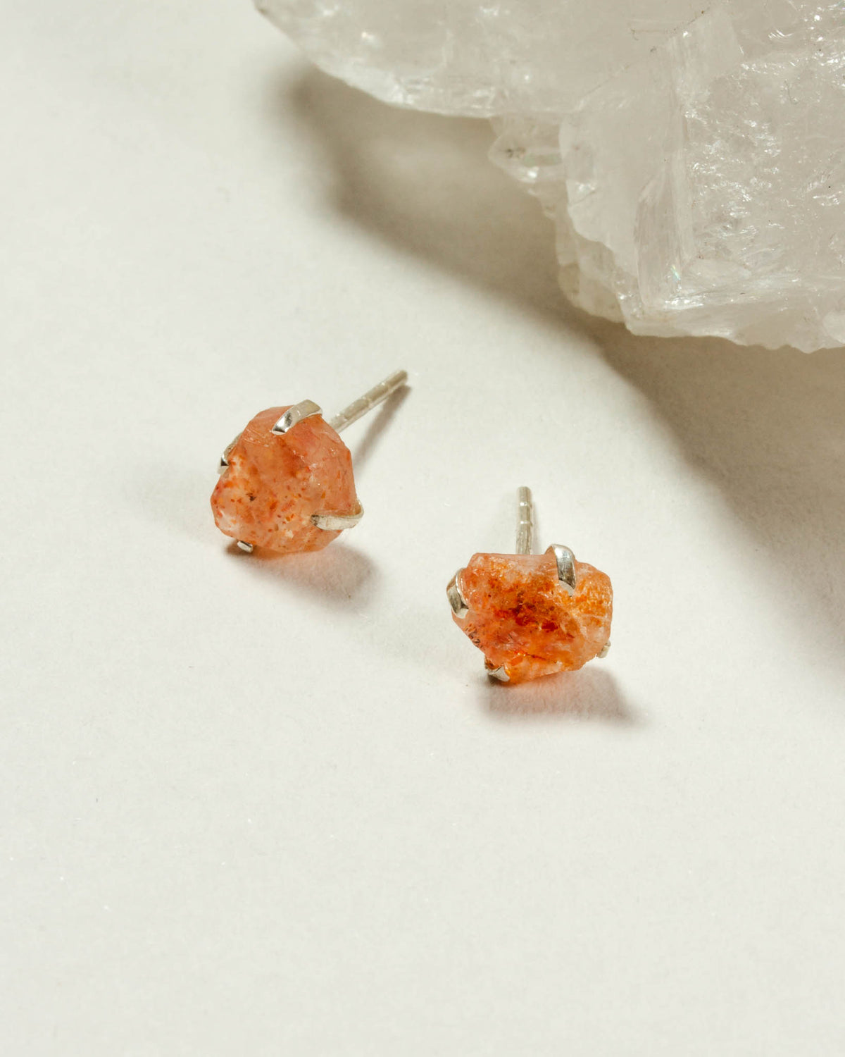 Sterling silver post earrings with raw sunstone gems are displayed on a white surface.
