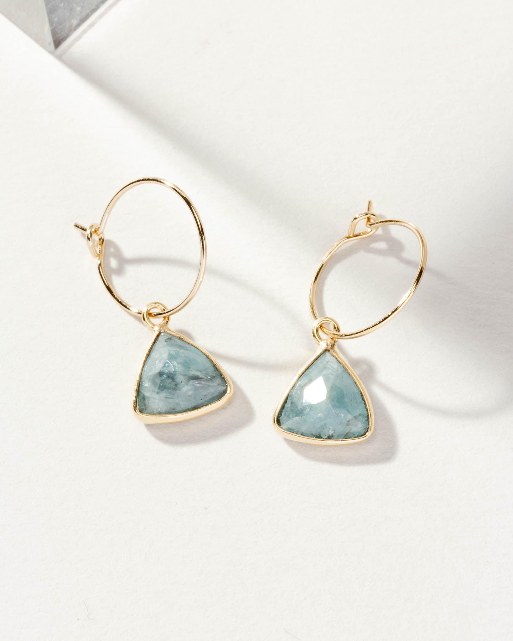 Pair of gold mini hoop earrings with aquamarine triangle stones.