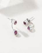Two silver Double Trouble earrings with bezel set Amethyst gemstones, laying on a white surface.