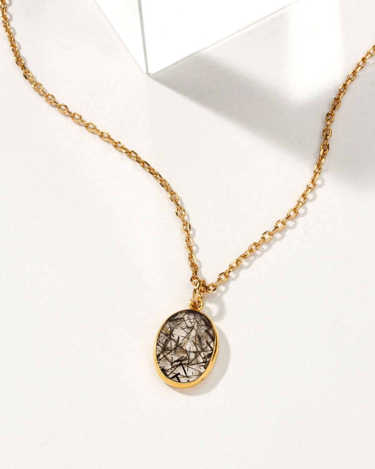 Gold chain necklace with oval tourmalinated quartz pendant.