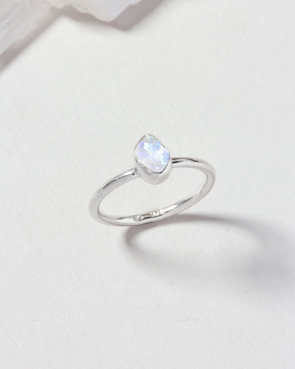 Silver ring featuring an iridescent moonstone teardrop on a white surface.