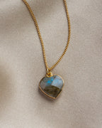 Close-up of labradorite heart-shaped charm necklace on a khaki background.
