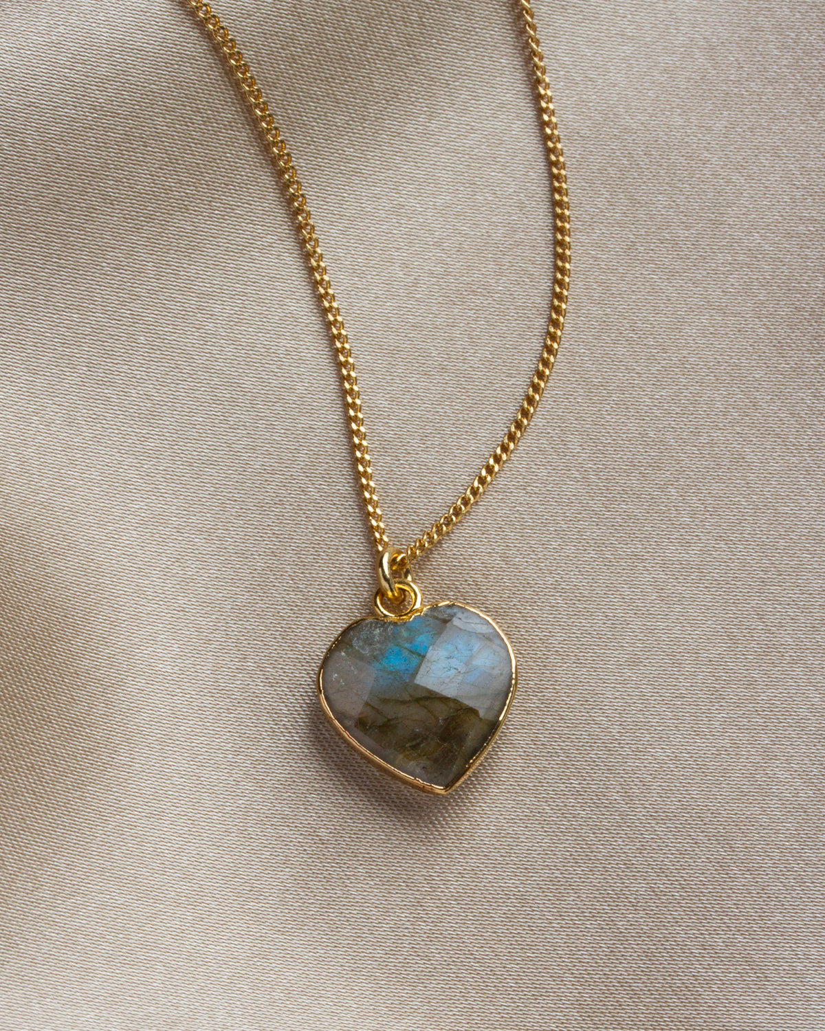 Close-up of labradorite heart-shaped charm necklace on a khaki background.