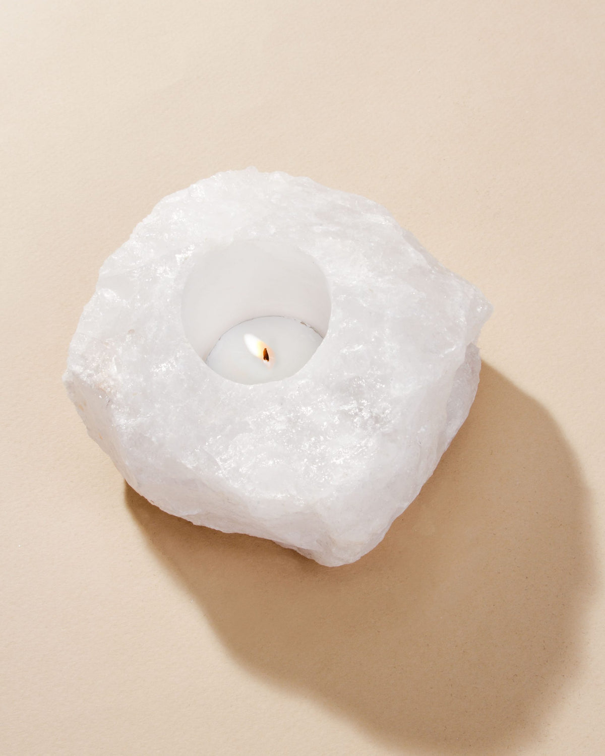 Quartz candle holder with lit tea light, sitting on a tan surface.