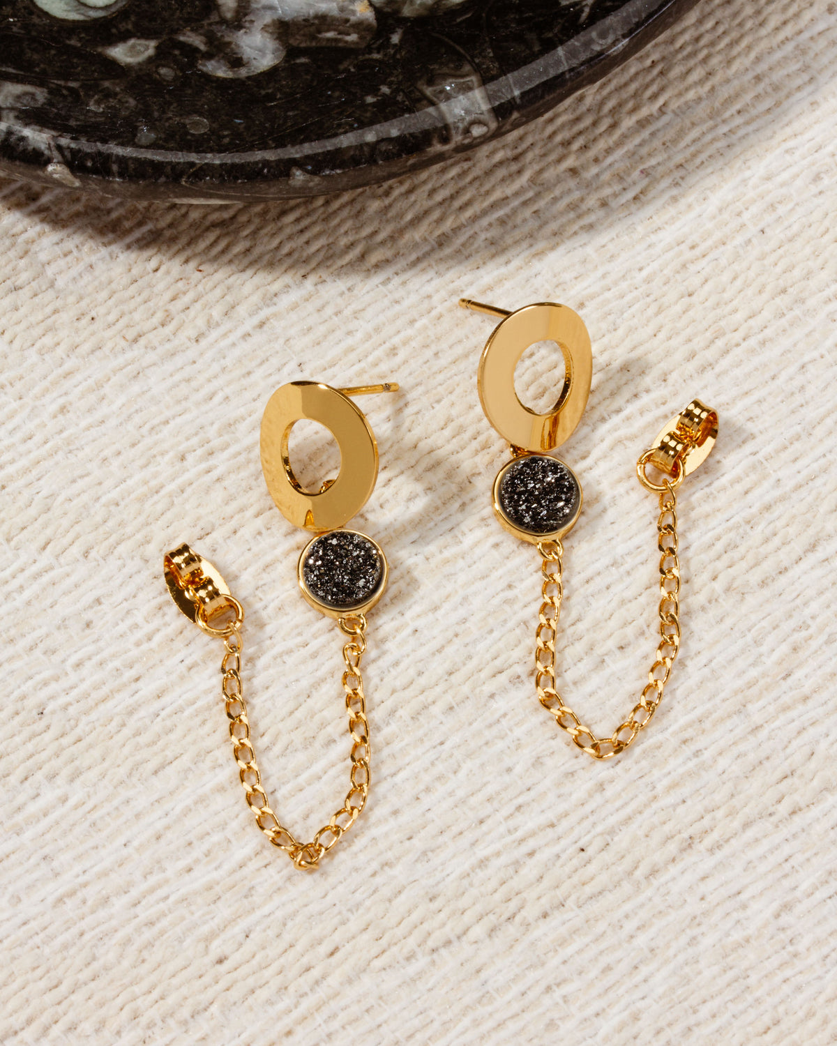 Earrings featuring gold open circles with black druzy quartz stones and dangling gold chains.