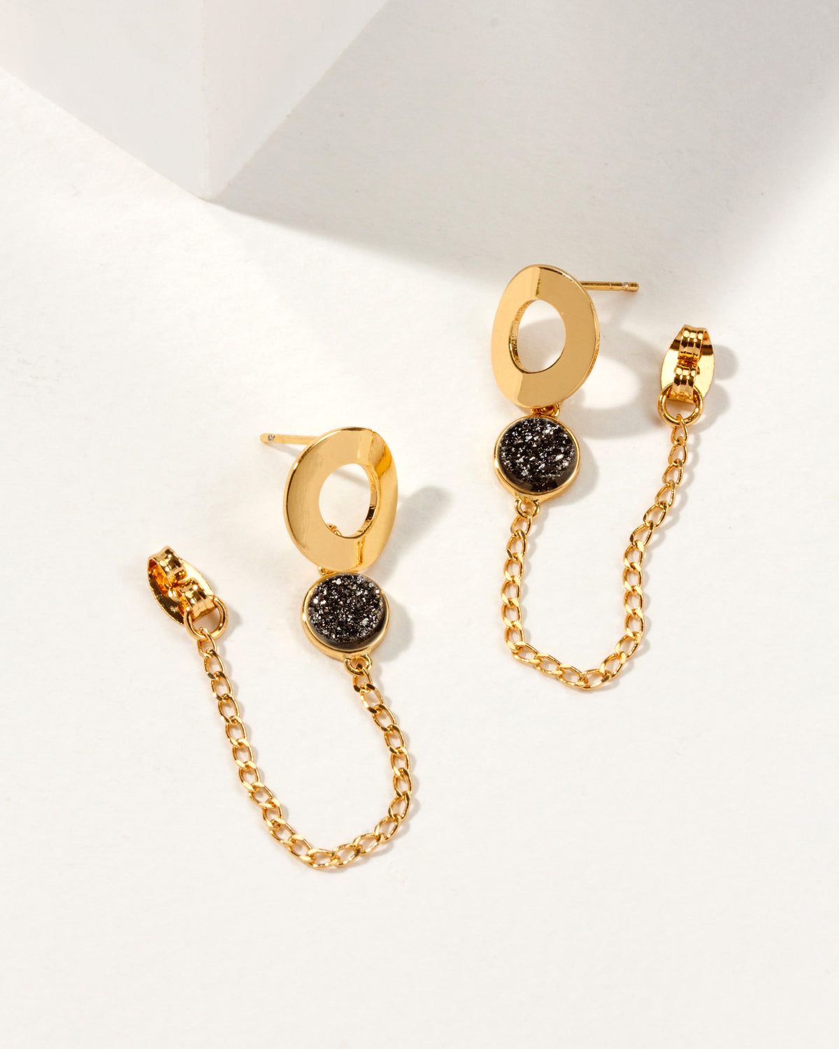 Earrings with gold circle, a black druzy quartz stone, and gold chain attached to the earring back.