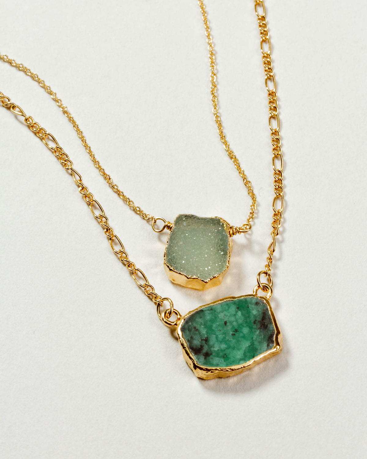Two-tiered gold chain necklace with an emerald and light green gemstone.