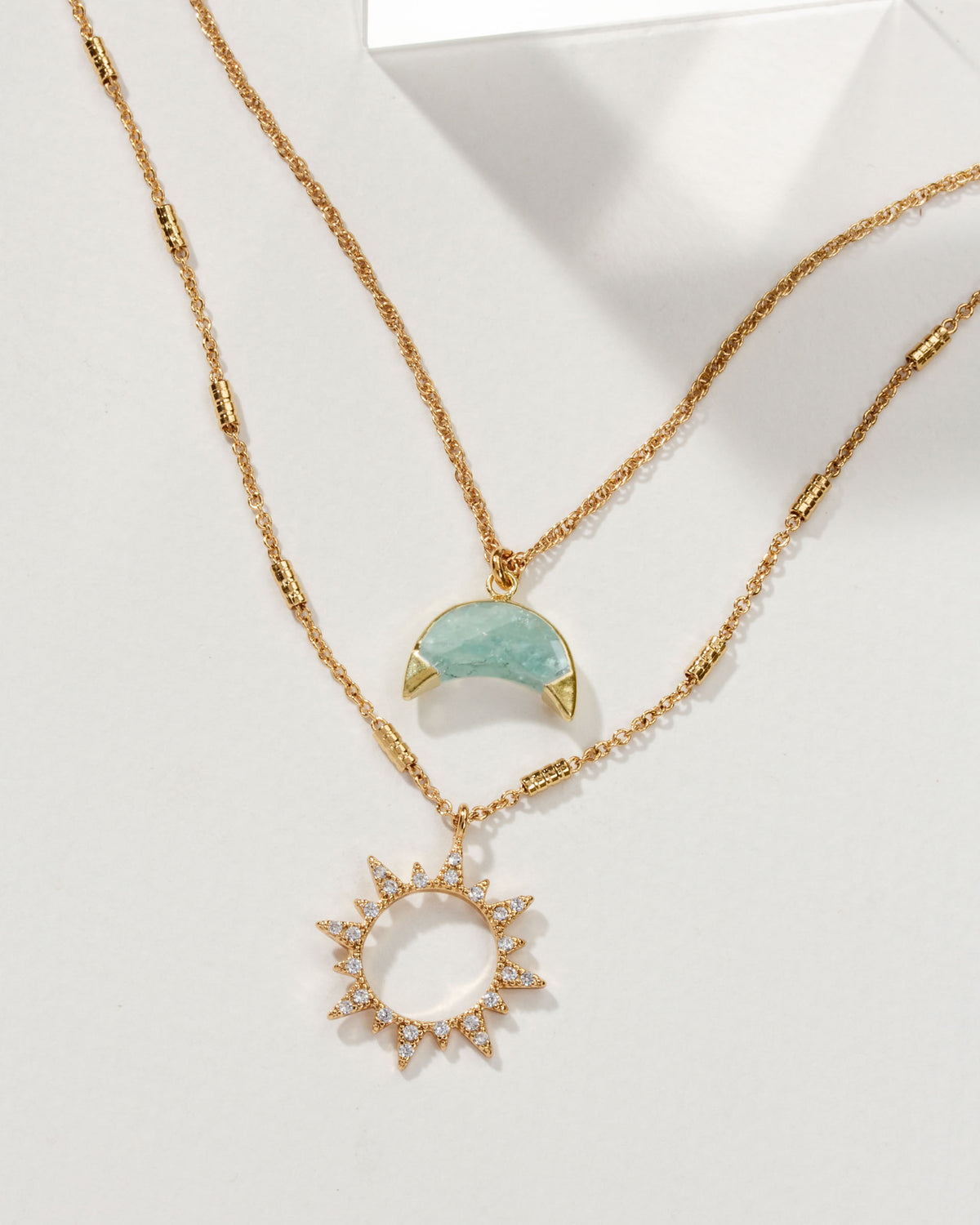 Gold necklace set with an Aquamarine moon pendant and a sun pendant with white gemstones.