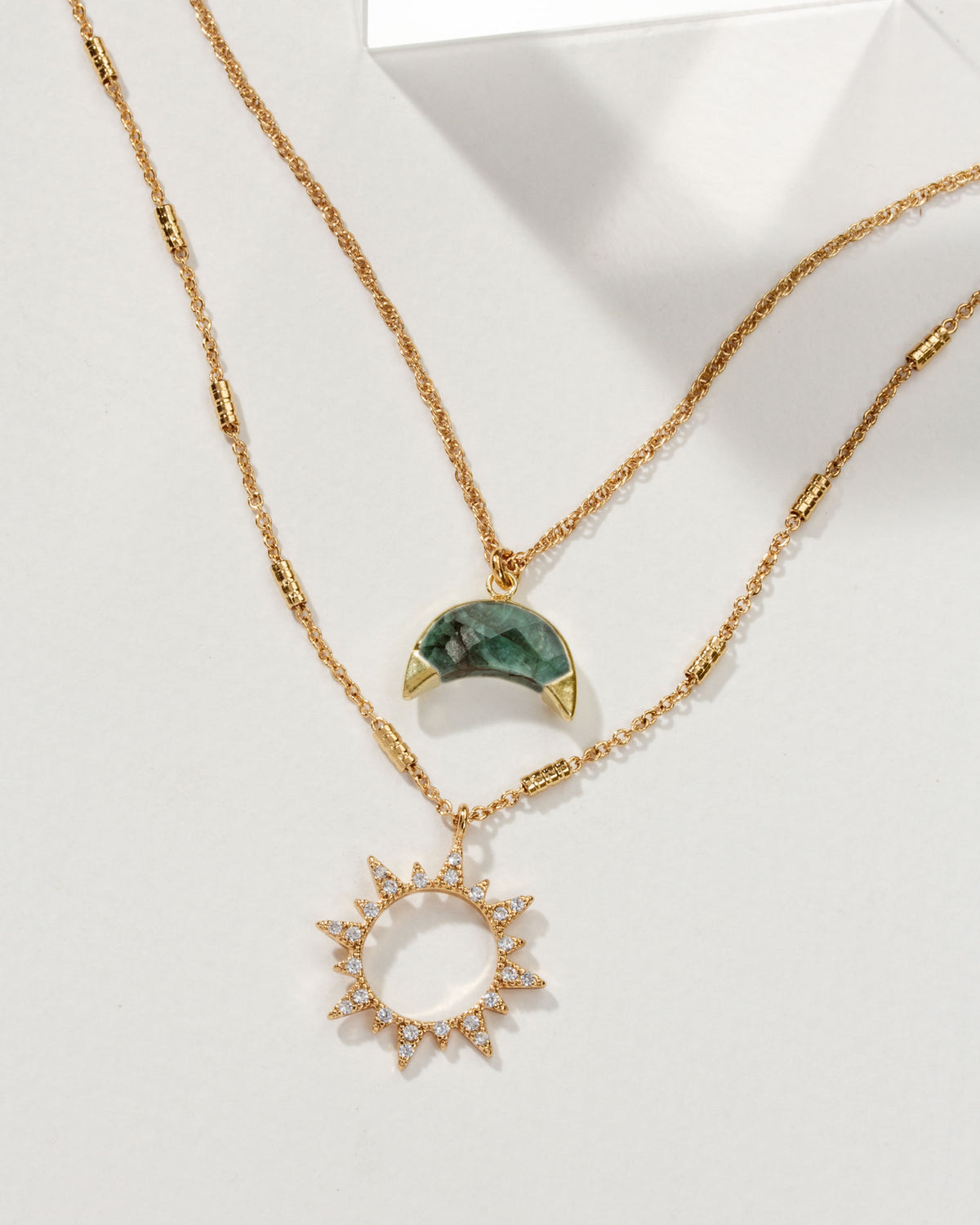 Gold necklace set with emerald crescent moon and jeweled sun pendants.