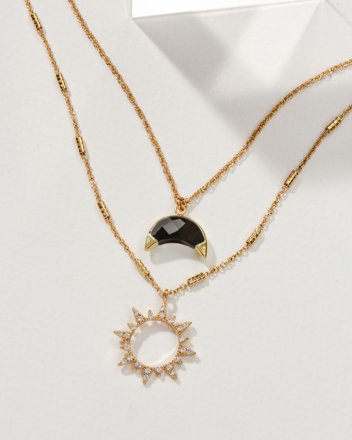 Gold necklace set with a sun pendant with stones and a moon pendant with Onyx.