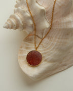 Gold chain necklace with strawberry quartz medallion against a seashell.