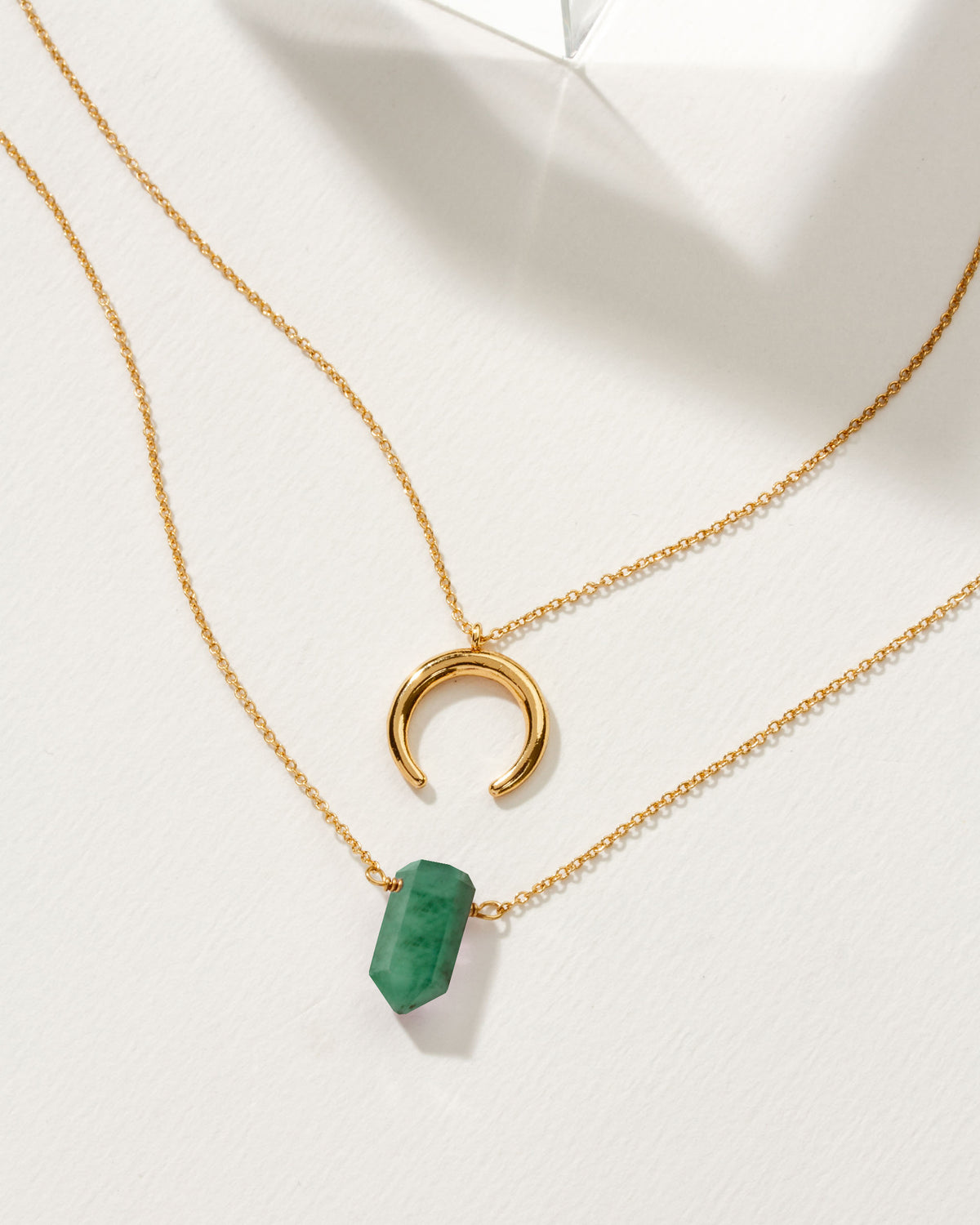 Layered gold necklaces, one with a green aventurine point and the other a crescent pendant.