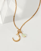 A gold chain necklace with a crescent moon and iridescent opal charm is displayed.