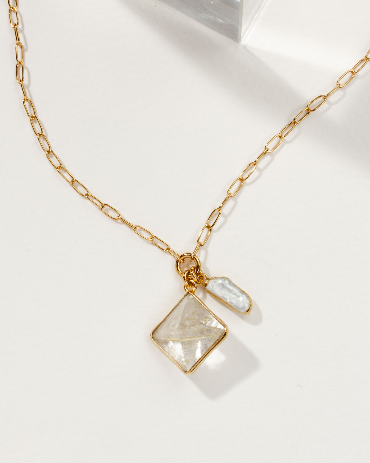 Gold chain necklace with rutilated quartz and white gemstone charms.
