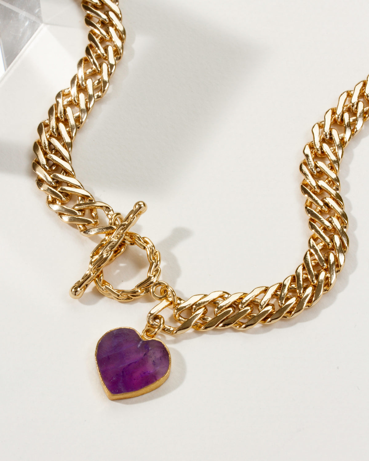 Gold chain necklace with a toggle closure and amethyst heart-shaped pendant.
