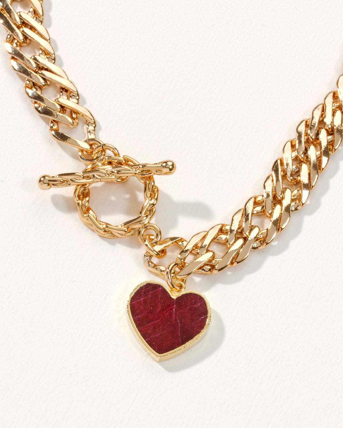 Gold chain necklace with a toggle clasp and a heart pendant featuring a ruby gemstone.