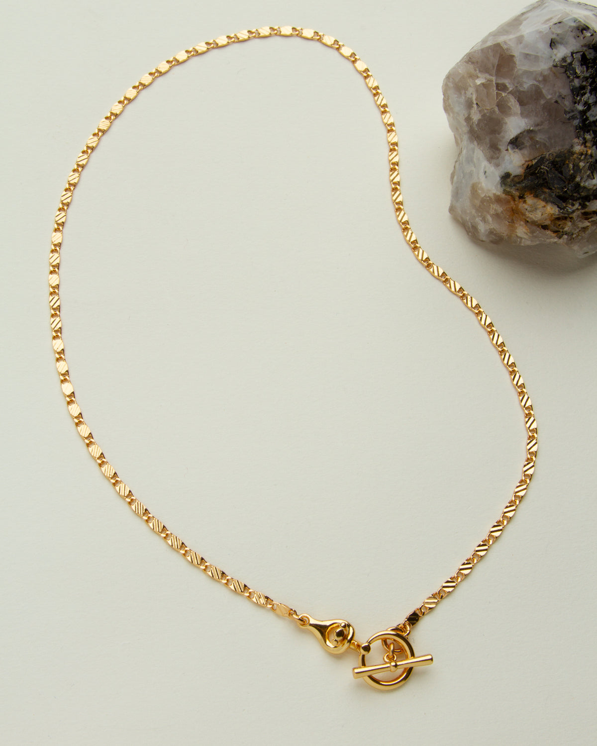 The Adorned Toggle Necklace features a delicate gold chain and a toggle clasp closure.