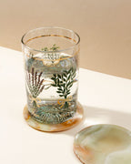 Tall glass of water sits atop an "On The Rocks Calcite Coaster" and another coaster sits beside it.
