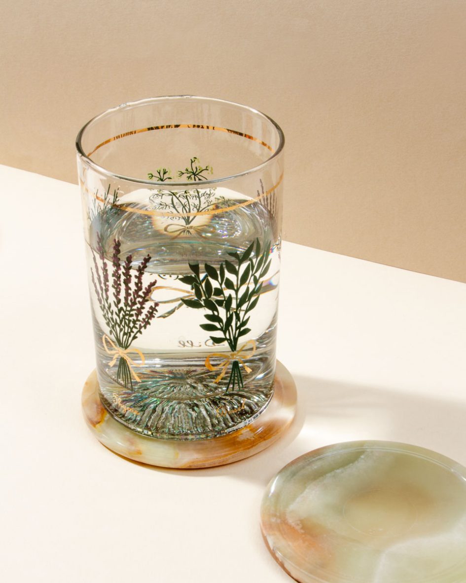 Tall glass of water sits atop an "On The Rocks Calcite Coaster" and another coaster sits beside it.