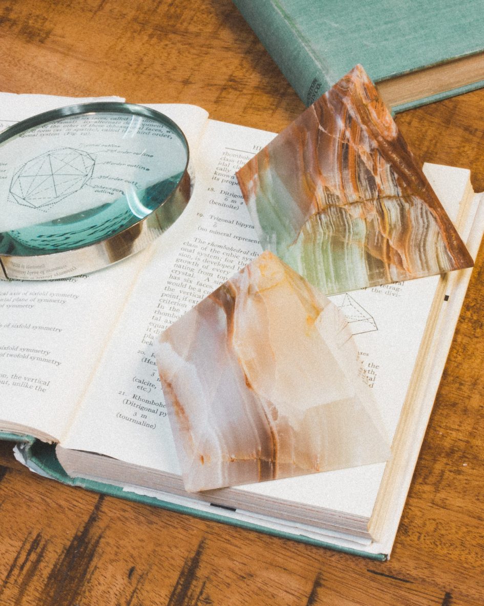 Two Wonder of the World Calcite Pyramids rest on an open book next to a magnifying glass.