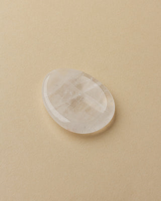 A smooth quartz stone with a slight indent, placed on a white surface.