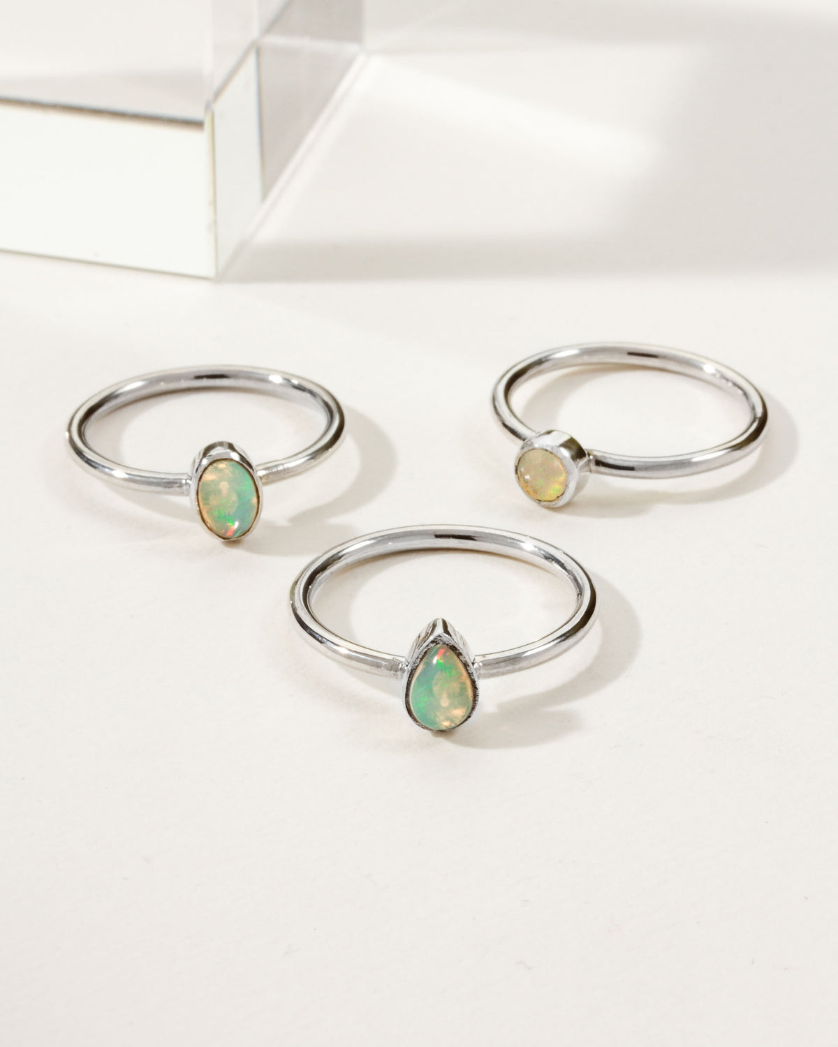 Three sterling silver rings with round, oval, and teardrop Play of Color Opal stones.