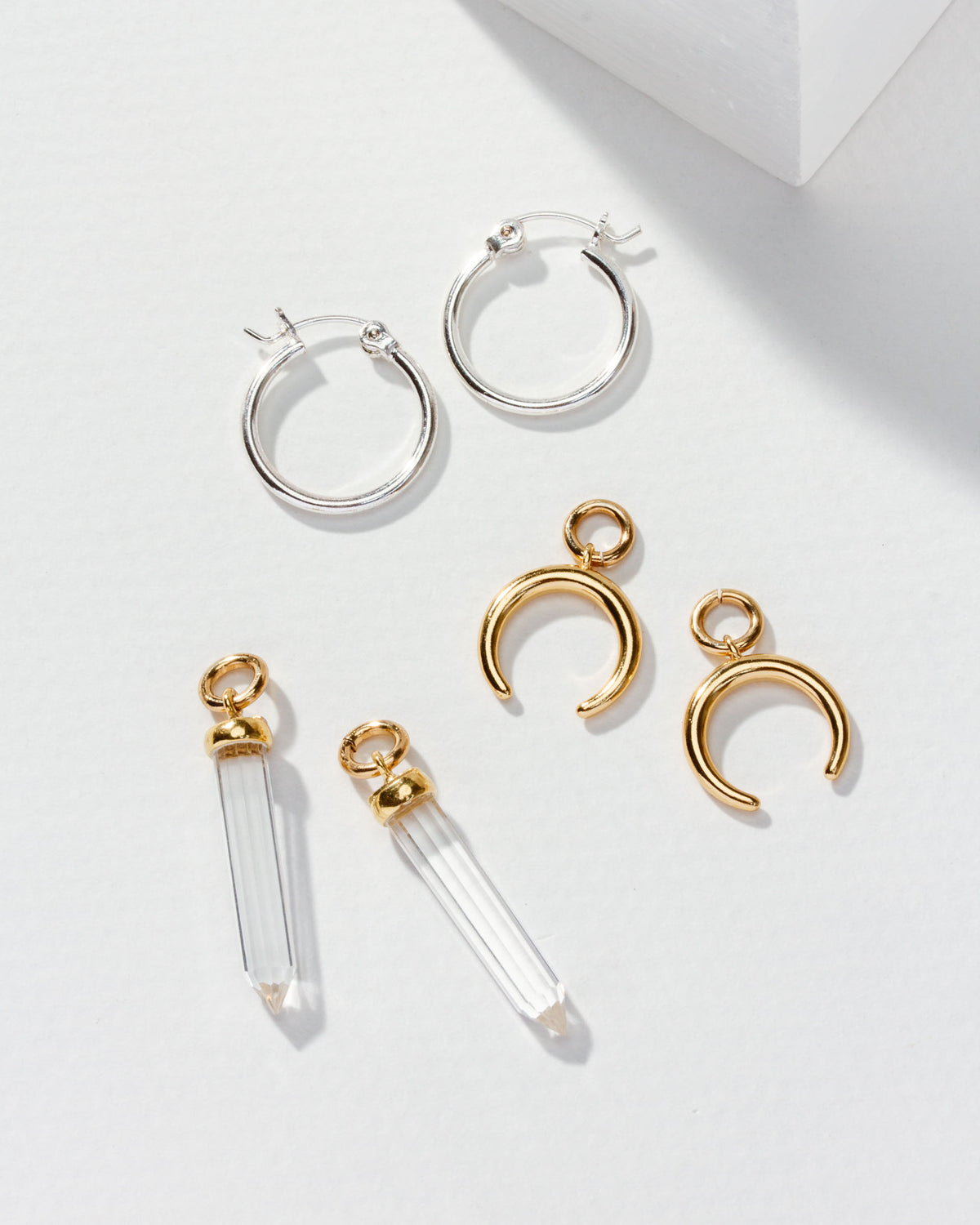 Silver hoops, gold crescent charms, and clear quartz points with gold caps, all scattered