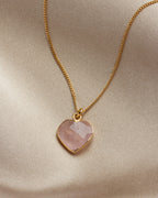 Rose quartz heart-shaped charm necklace on a khaki cloth background.