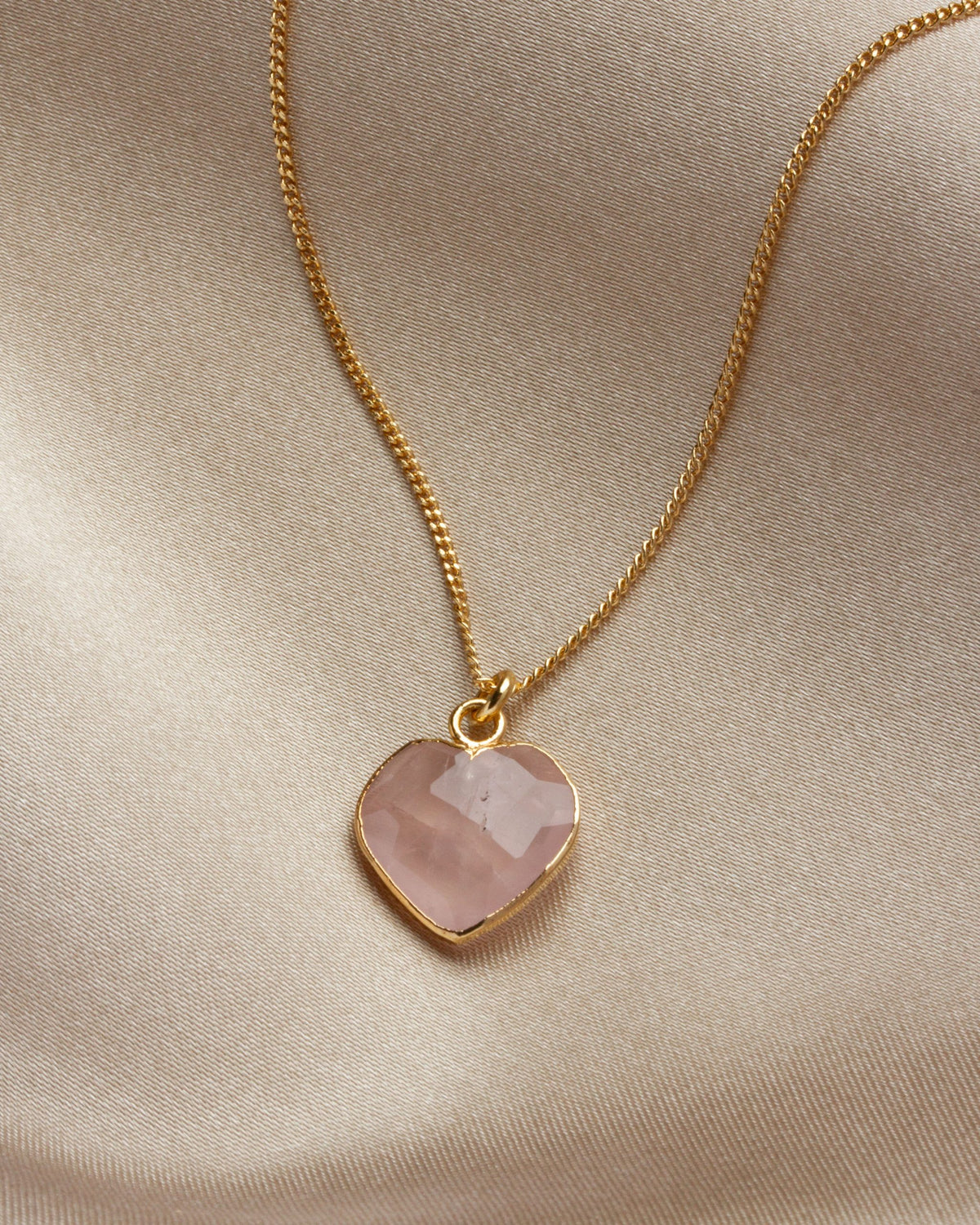 Rose quartz heart-shaped charm necklace on a khaki cloth background.
