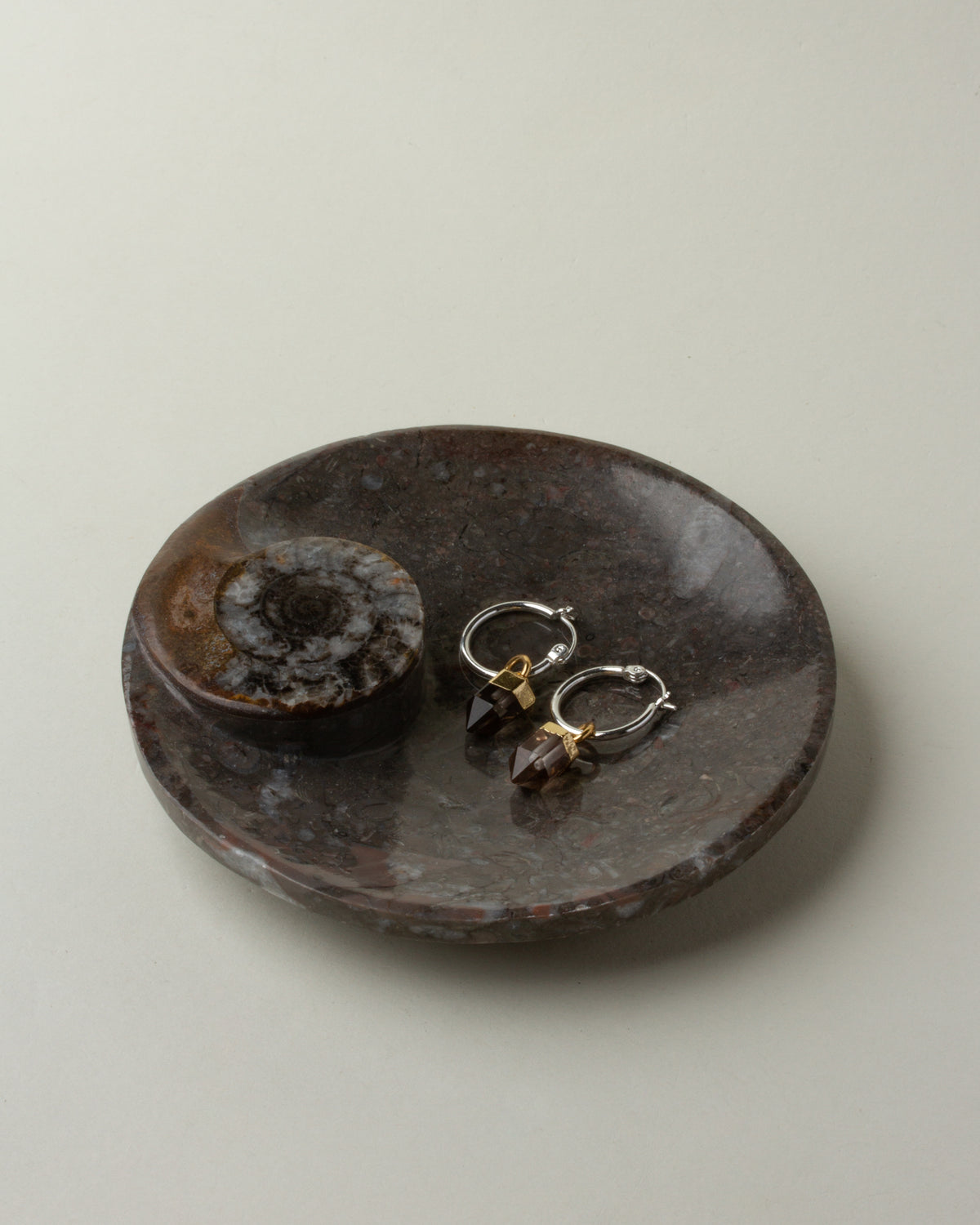 Brown Journey of Life catchall with earrings inside, sitting on a white surface.