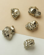 Five Fool Me Once Pyrite Nuggets are displayed on a divided beige and white background.